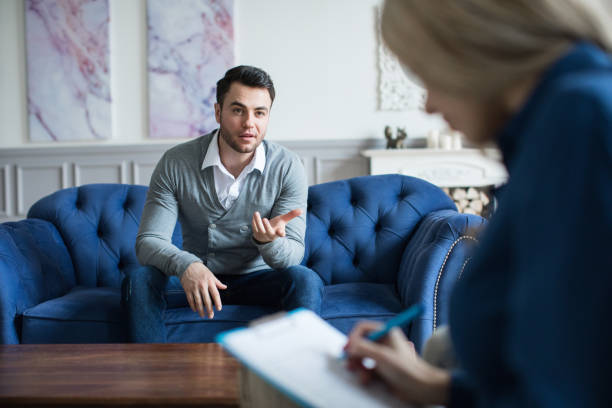 A man sits on the couch nd talking to a psychologist consultant.